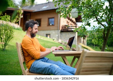 Side view of man with laptop working outdoors in garden, home office concept. - Shutterstock ID 1836342916