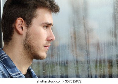 Side View Of A Man Longing And Looking Through Window In A Sad Rainy Day