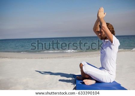 Side view of man meditating while sitting on exercise mat at beach