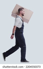 Side View. A Man In Overalls Carries A Large Cardboard Box