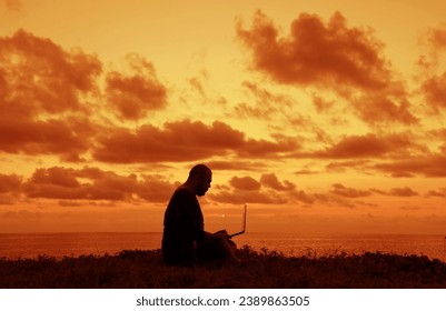 Side view of man silhouette using and looking at laptop computer during sunset over the ocean. male sitting on green grass. Silhouette of Man talking in screen when sun rising up. sun rays. sunlight. - Powered by Shutterstock