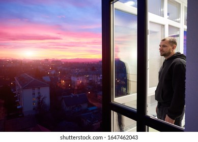 Side view of a man standing on a balcony with panoramic windows and looking into the distance while enjoying magical sunset. Urban landscape from height and a multi-colored fiery sky with setting sun - Shutterstock ID 1647462043