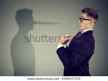Side view of man in suit pointing at himself looking at shadow with long nose of a liar. 