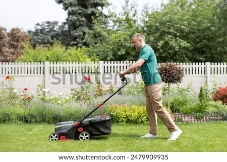 Side view of man using lawn mower cutting the grass in the backyard. Modern agricultural machinery for the care of the garden