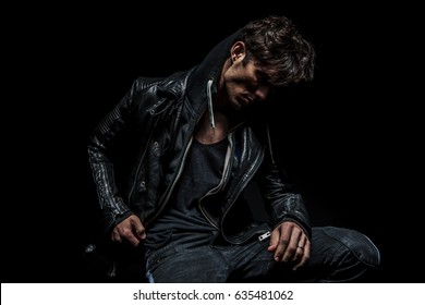 side view of a man wearing hoodie and leather jacket looks down on black background