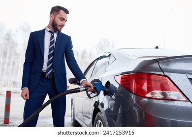 Side view at man wearing suit while refueling gas tank of car in petrol station, copy space - Powered by Shutterstock