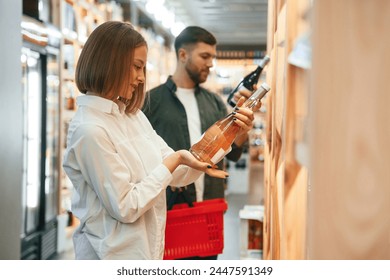 Side view. Man and woman are choosing wine in the shop.