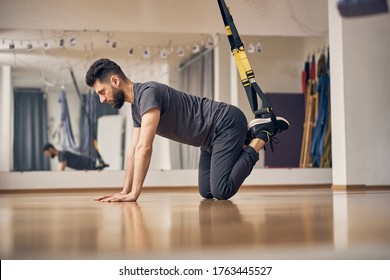Side view of a man working out with bent knees and his feet in the training loops