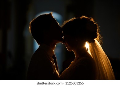 Side View Of Married Couple In Darkness. Groom Is Kissing A Bride In Her Forehead, With The Light Of Lanterns. Silhouette Of Wedding Couple