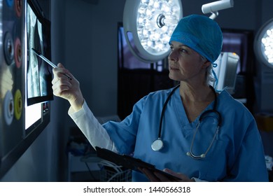 Side view of mature Caucasian female surgeon examining x-ray while writing on clipboard in operating room of hospital