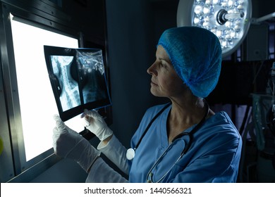 Side view of mature Caucasian female surgeon examining x-ray on light box in operating room of hospital - Powered by Shutterstock