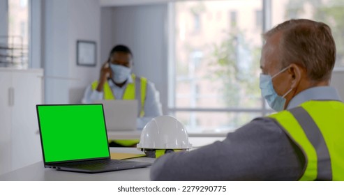 Side view of mature constructor in safety mask having video chat on laptop. Green screen. Man architect in face mask have video conference with engineering team working in office - Powered by Shutterstock