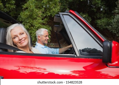 Side View Of Mature Couple Driving Red Convertible On Bright Day