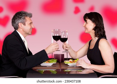Side view of mature couple toasting wineglasses at table in restaurant
