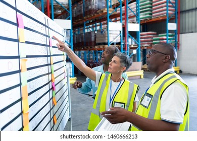 Side View Of Mature Diverse Warehouse Staffs Discussing Over Whiteboard In Warehouse. This Is A Freight Transportation And Distribution Warehouse. Industrial And Industrial Workers Concept