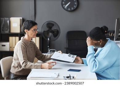 Side view of mature female manager passing rejected visa application form to anxious black woman touching her head while feeling upset - Shutterstock ID 2389002507