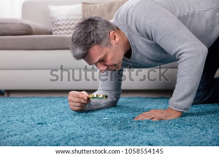 Side View Of A Mature Man Looking At Blue Carpet Through Magnifying Glass