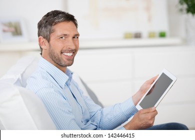 Side View Of Mature Man Reading Ebook At Digital Tablet While Sitting On Sofa At Home