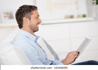 Side View Of Mature Man Reading Ebook At Tablet Pc While Sitting On Sofa At Home