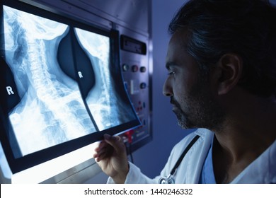 Side View Of Mature Mixed Race Male Doctor Examining X-ray On X-ray Light Box In Operation Room At Hospital