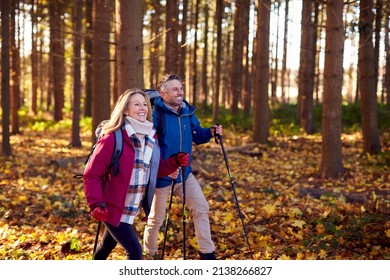 Side View Of Mature Retired Couple Walking Through Fall Or Winter Countryside Using Hiking Poles