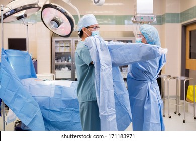 Side View Of Mature Scrub Nurse Assisting Surgeon Putting On Sterile Operating Gown