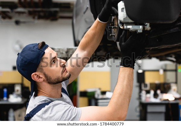 side view of mechanic in cap and rubber gloves\
fixing vehicle