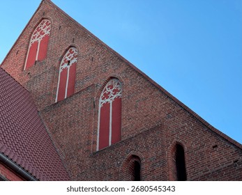 Side view of medieval gothic brick church built in 1370 in Europe, with pointed arched windows and red painted details against blue sky.