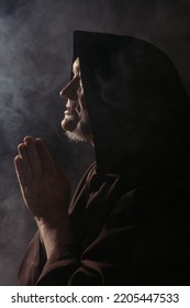 Side View Of Medieval Monk In Hooded Robe Praying On Black With Smoke