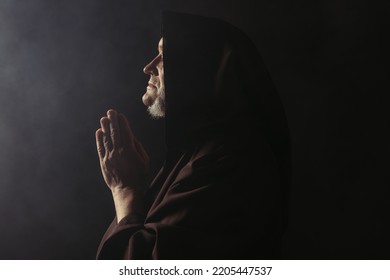 Side View Of Medieval Monk In Hooded Robe Praying On Black With Smoke