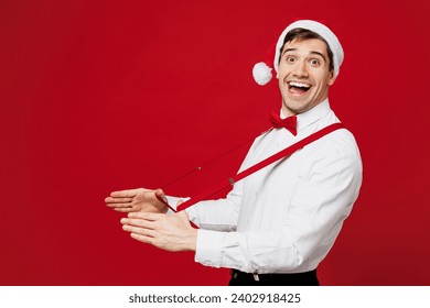 Side view merry smiling young man wear white shirt Santa hat posing look camera hold suspenders isolated on plain red background studio portrait. Happy New Year Christmas celebration holiday concept - Powered by Shutterstock