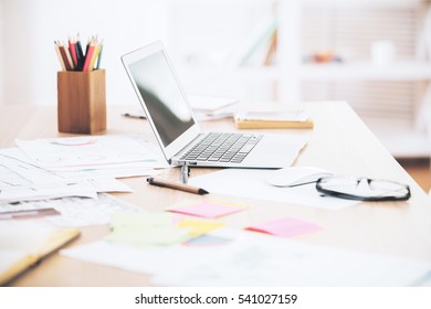 Side View Of Messy Office Desktop With Blank Laptop And Supplies