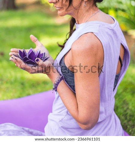 Side view of mid adult woman holding a purple glass lotus. Yoga and meditation concept.