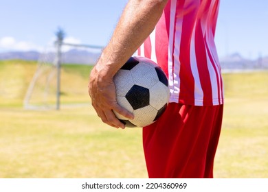 Side View Mid Section Of A Caucasian Male Football Player Wearing A Team Strip, Training At A Sports Field In The Sun, Holding A Football During A Break, With Blue Sky In The Background