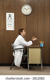 Side View Of Mid-adult Caucasian Male Doctor Sitting At Desk.