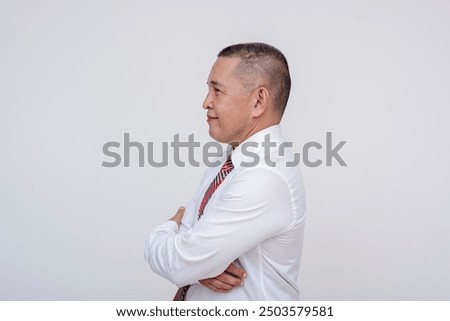 Side view of a middle aged asian businessman or manager with arms crossed. Wearing a striped red necktie and buzz cut hairstyle.