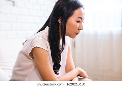 Side View Of Middle Aged Beautiful Asian Woman Sitting Crying And Wiping Out Tears And Thinking About Problems Indoors