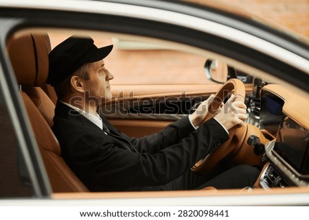 Side view of middle aged Caucasian chauffeur driving luxury car, focusing on passenger transport service and executive mobility. Ideal for travel, business transport, premium service ads
