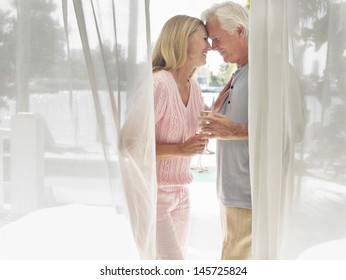 Side View Of A Middle Aged Couple With Champagne Flutes Behind Curtain