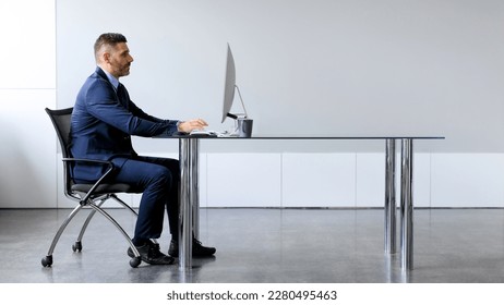 Side view of middle aged male manager working on computer in office, sitting at desk and using pc, looking at screen, panorama with free copy space - Shutterstock ID 2280495463