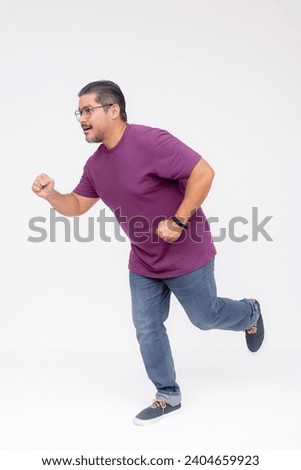 Side view of a middle aged man running towards the camera at full speed. Wearing a purple waffle shirt and jeans. Full body photo, isolated on a white background.