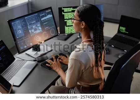 Side view of Middle Eastern female IT engineer typing on keyboard developing computer software while sitting at professional workstation in office