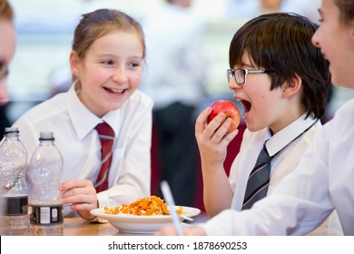 Side View Of A Middle School Students Eating An Apple During Lunch In The School Cafeteria.