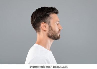 Side view of middle-aged bearded man in white t-shirt over grey studio background, copy space. Profile portrait of handsome man with closed eyes posing on gray, standing straight and looking aside