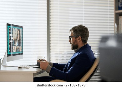 Side view of middle-aged bearded manager having video conference with foreign female colleague while sitting at office table