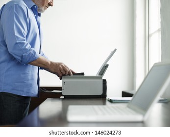 Side view midsection of a mature man using printer at study table in house - Powered by Shutterstock