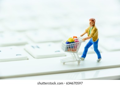 Side View Of Miniature Figurine :a Shopper Pushes A Shopping Cart On A White Keyboard. Concept Of Brick And Mortar Stores Nowadays Face A Giant Wave Of Store Closure Due To Decreasing In Foot Traffic.