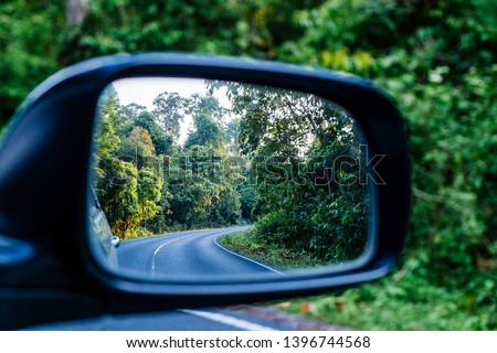 Side view mirror reflection of curve road in the forest.