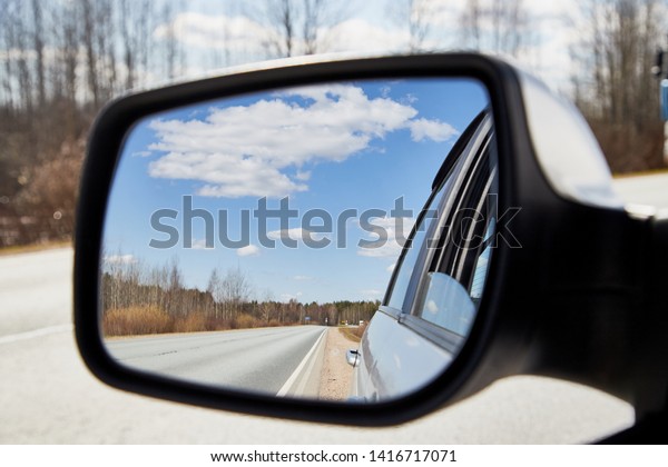 Side view mirror reflection of landscape\
with road and sky with clouds in sunny spring or autumn day. Russia\
and russian nature during travel by\
car