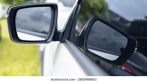Side View Mirror Reflection on a Rainy Day,Close-up shot of a modern car side view mirror capturing reflections of a cloudy sky and surrounding environment after the rain, with water droplets visible on the glass surface.